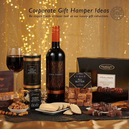 Corporate gift hamper ideas from Spicers of Hythe featuring a wine gift sat on a table top surrounded by chocolate and savoury treats.