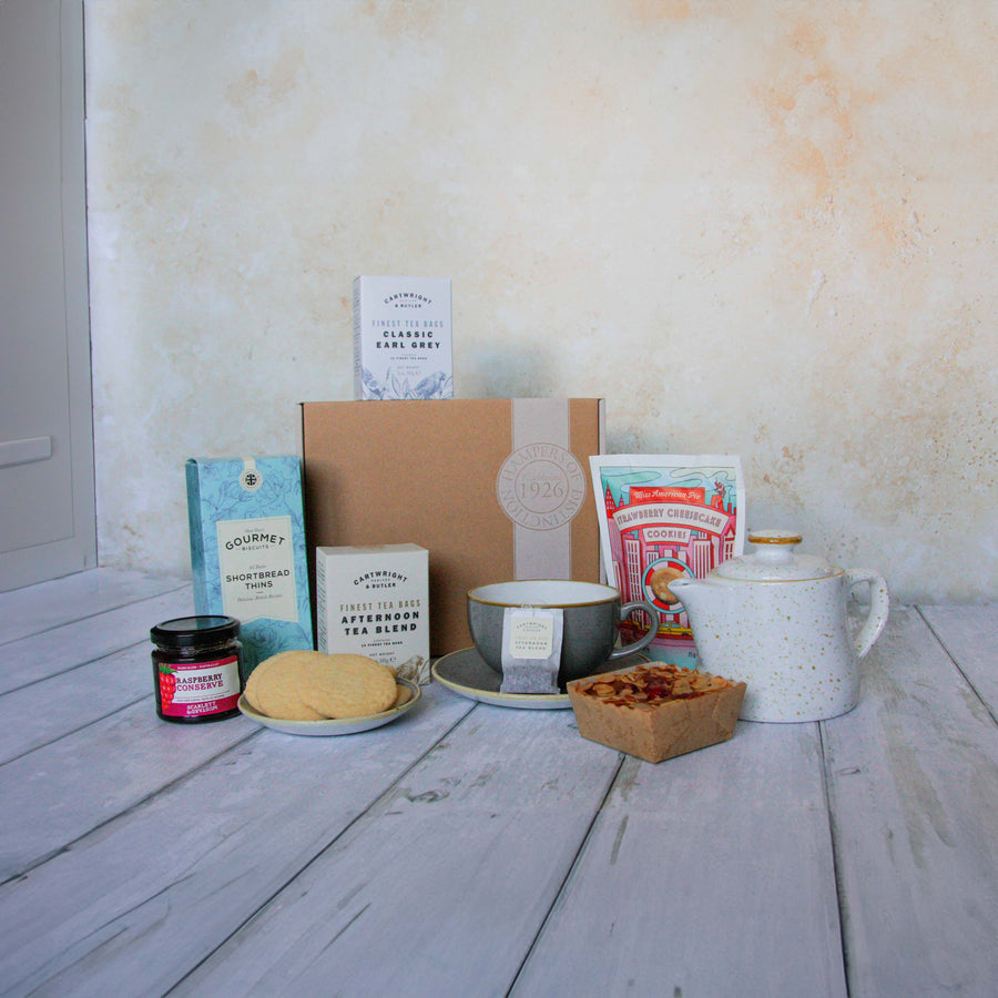 The contents of the Afternoon Tea Hamper laid out on a wooden table top with a pale wall in the background.